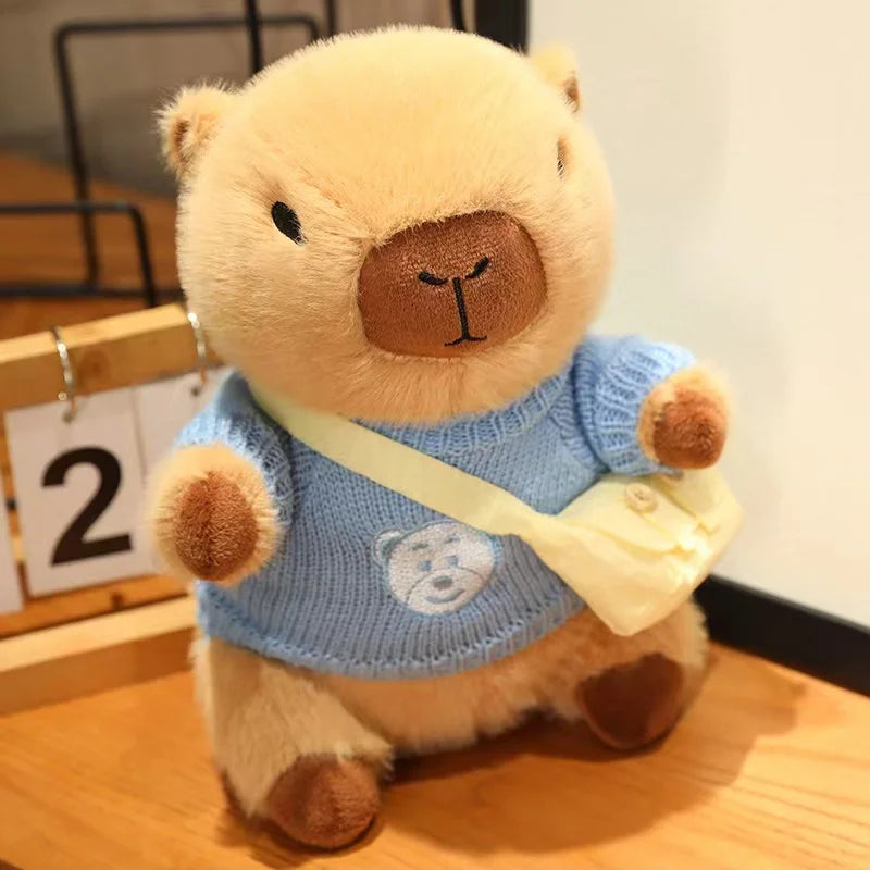 Kawaii teddy bear wearing a blue sweater with a white strap on a wooden surface.