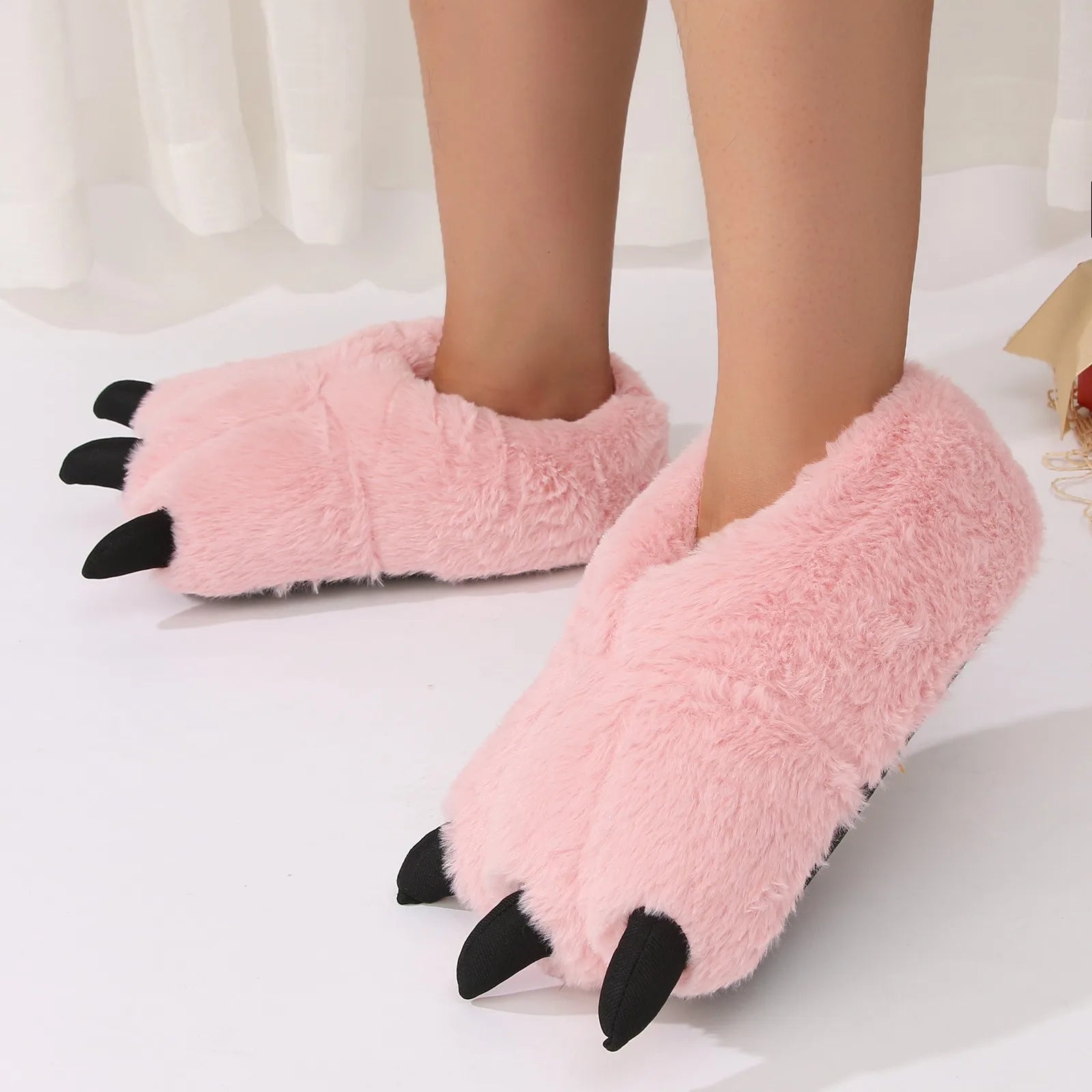 Pink fuzzy kawaii slippers with black claw-like accents worn by a person on a white background