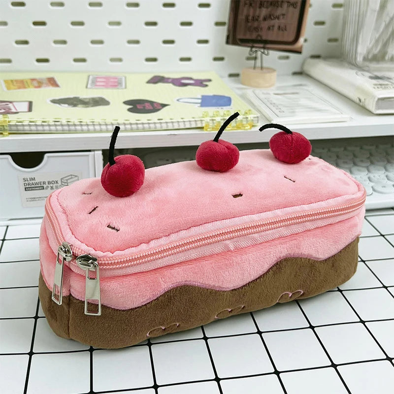 Pink and brown kawaii pencil case shaped like a cake with cherries on top, placed on a checkered floor.