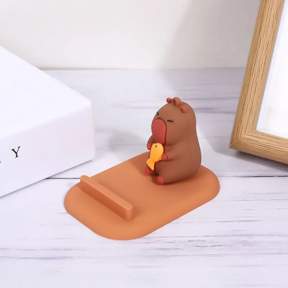 Brown kawaii capybara phone holder holding a yellow object on an orange stand with a white background