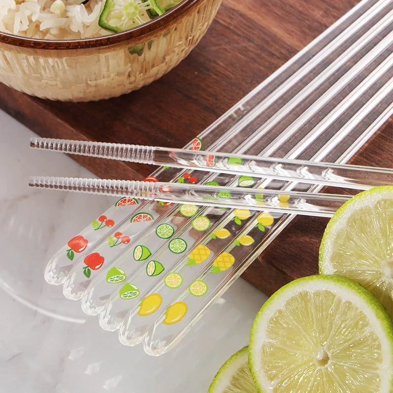 Clear kawaii chopsticks with fruit patterns on a wooden table with sliced limes and a bowl of rice.