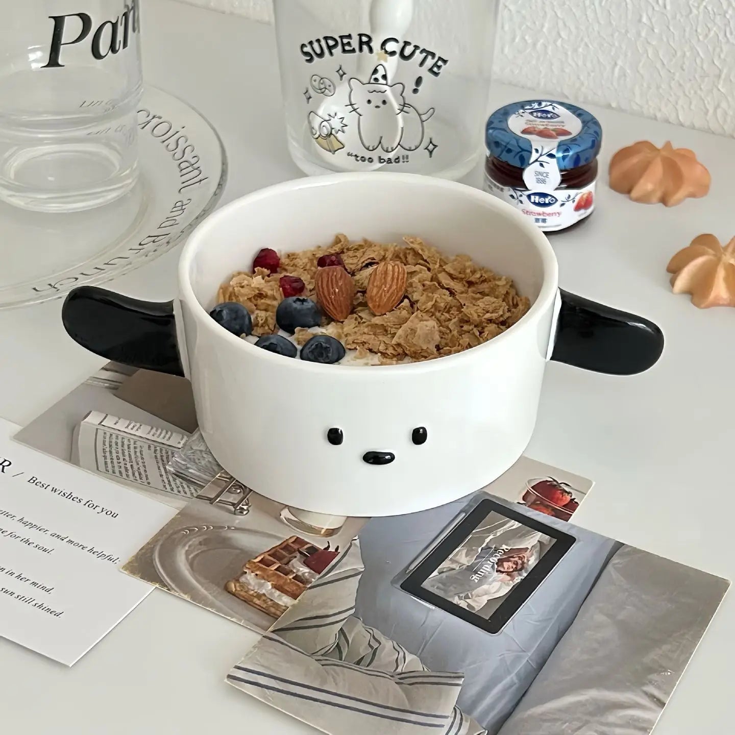 Cute animal-shaped kawaii ramen bowl with cereal and fruit on a table with glasses and a jar.