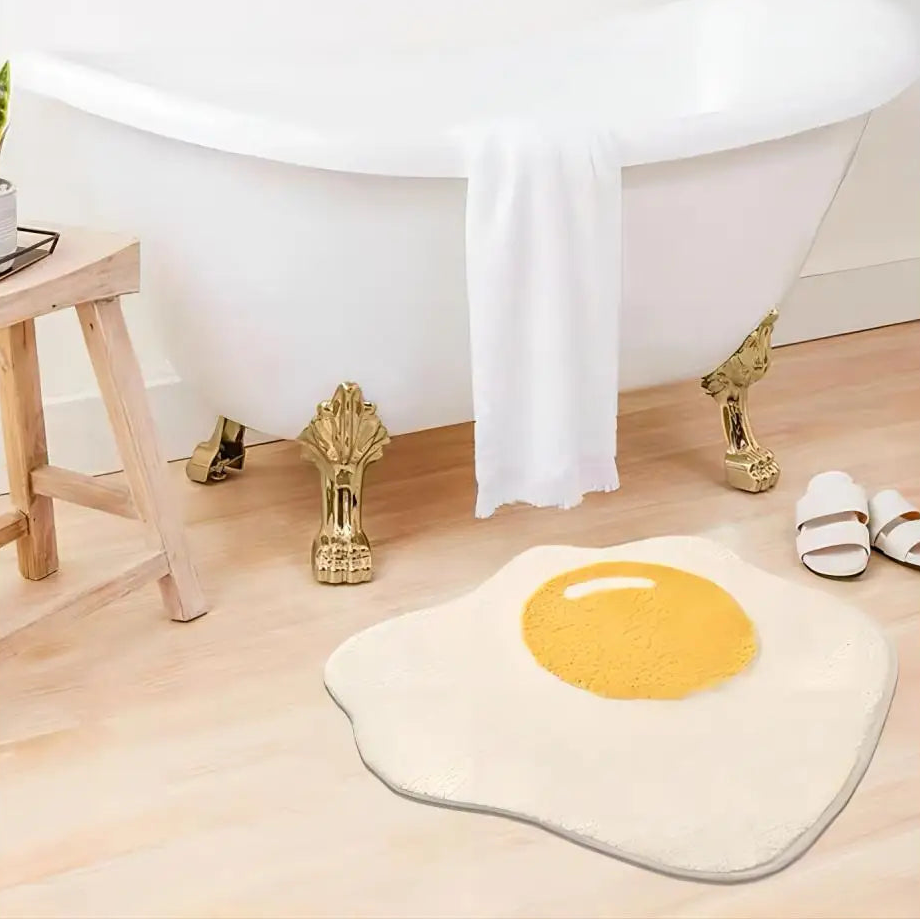 Fried egg-shaped kawaii rug on a wooden floor with a bathtub in the background.