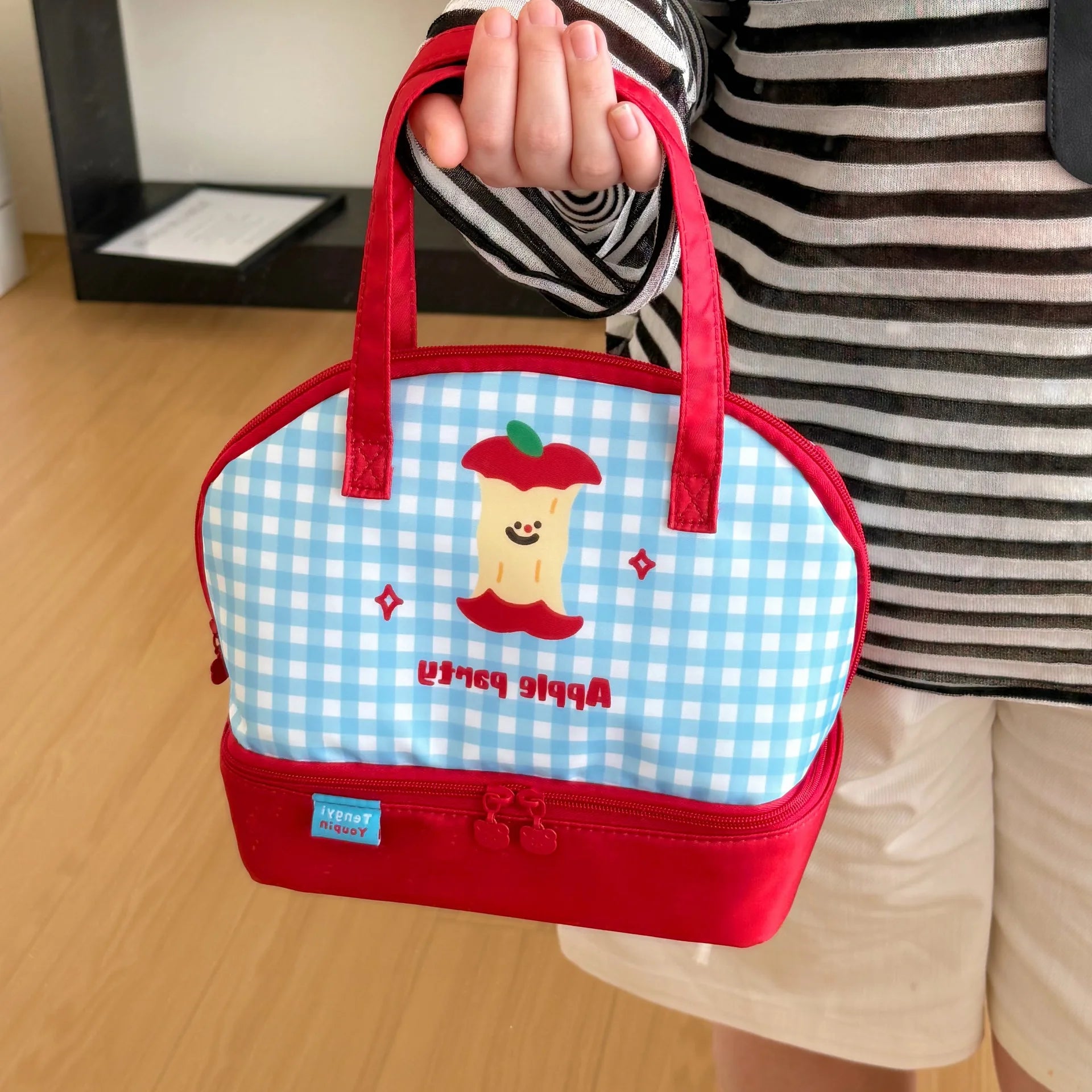 Person holding a small kawaii  lunch bag with a cartoon design on a wooden floor.