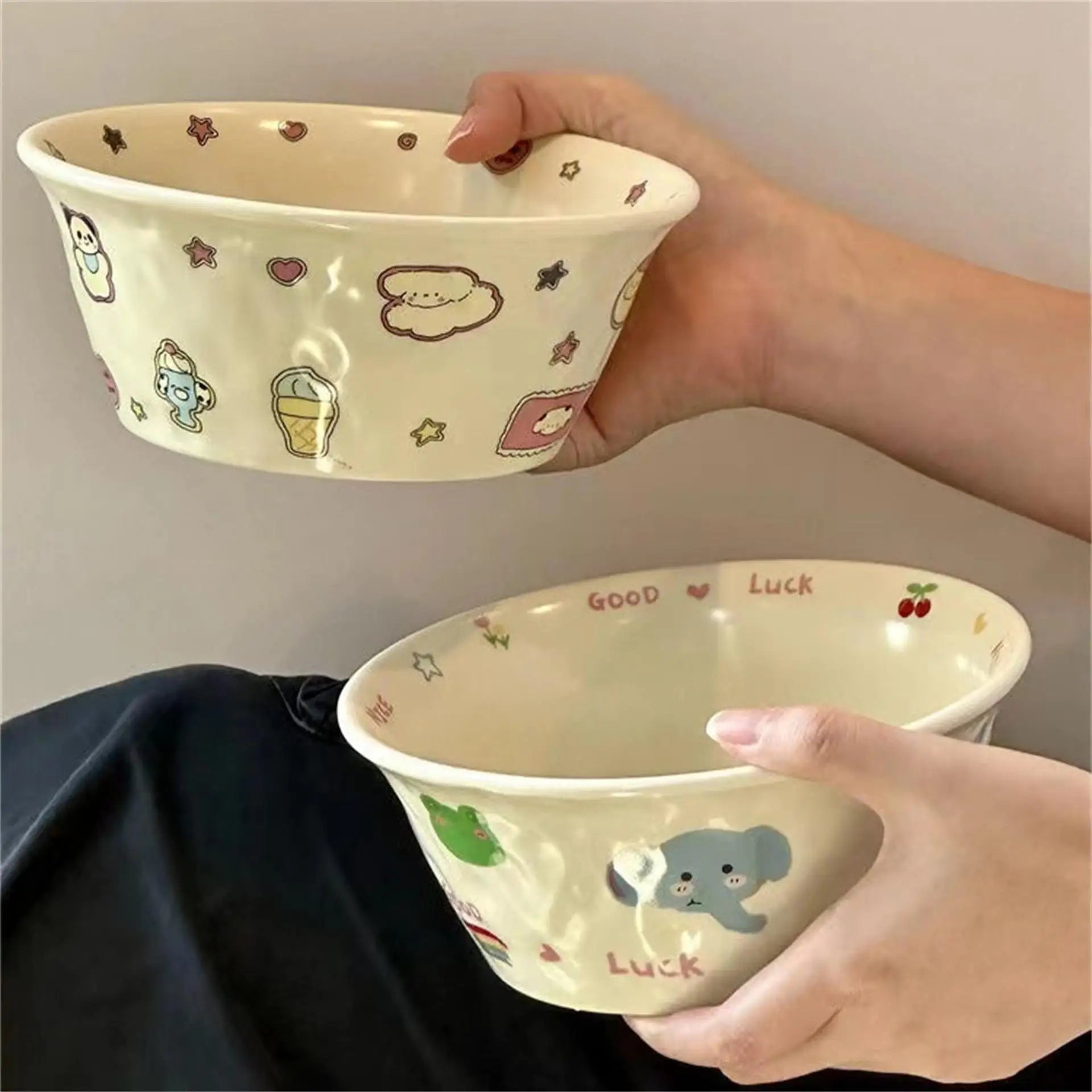 Two ceramic kawaii ramen bowls with cartoon designs held by hands against a neutral background