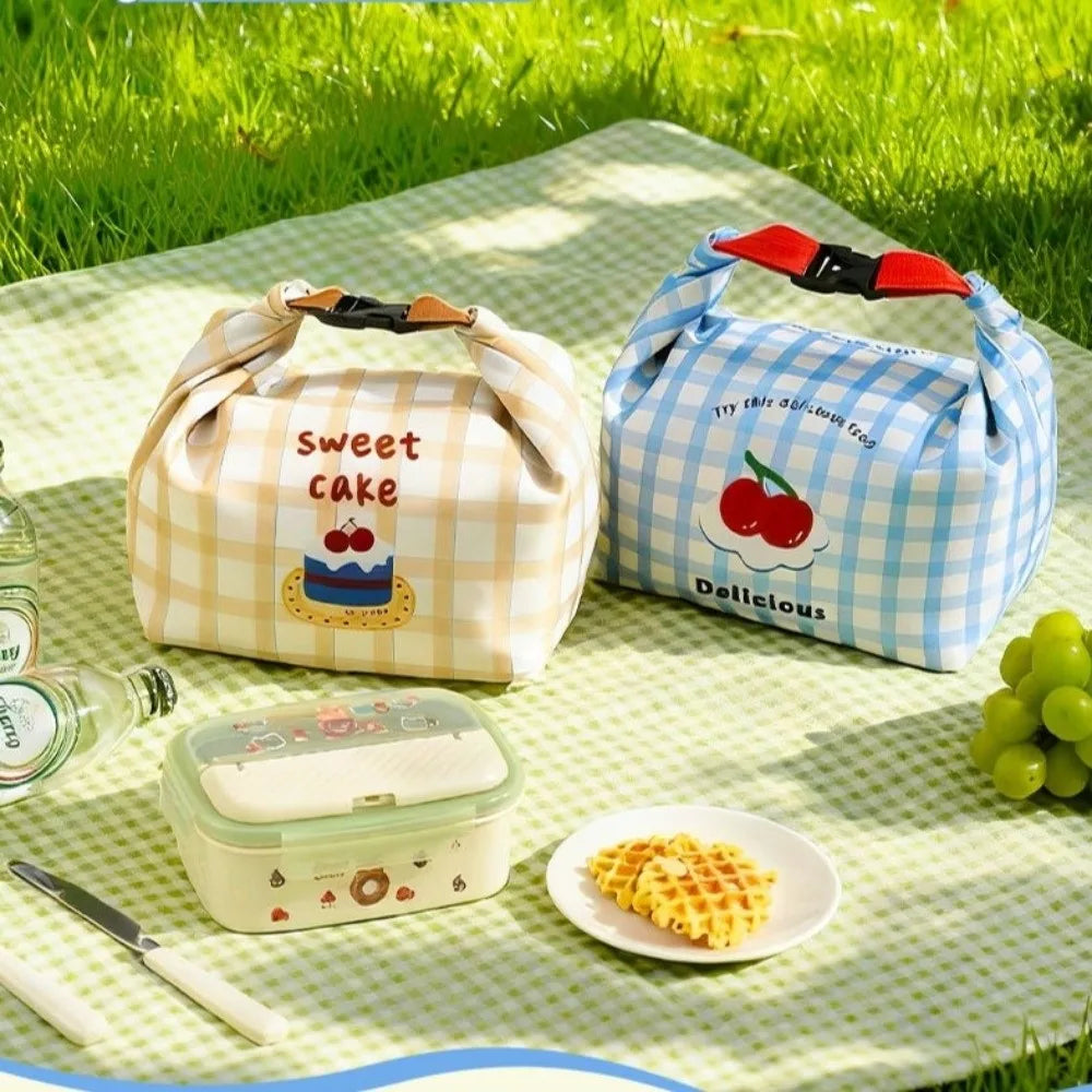 Two checkered kawaii lunch bags on a picnic blanket with food items and a bottle.