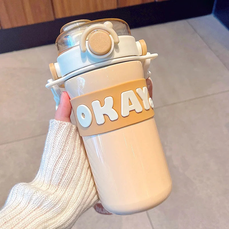 Beige kawaii water bottle with 'OKAY' text held by a person wearing white socks.