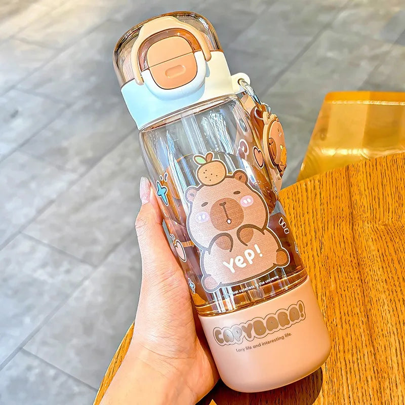 Clear kawaii water bottle with cartoon bear design held by a hand on a wooden surface.