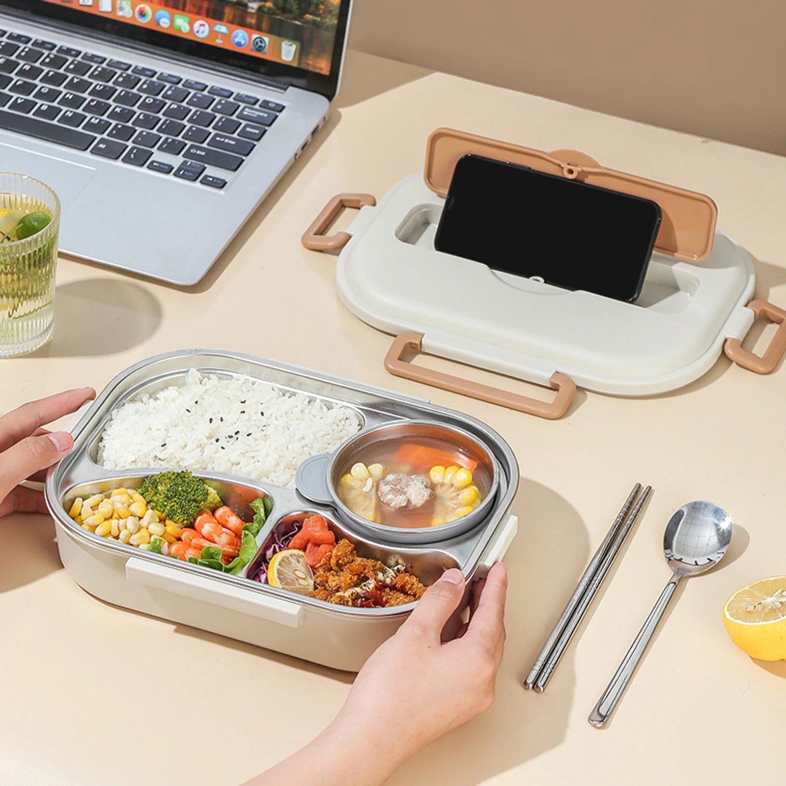 Kawaii bento box with compartments of food, smartphone, and laptop on a beige surface