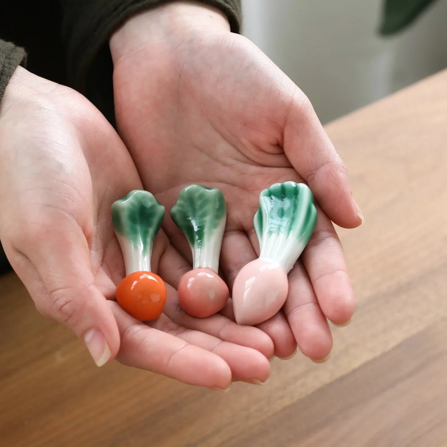 Hands holding ceramic vegetables kawaii chopstick holders on a wooden surface