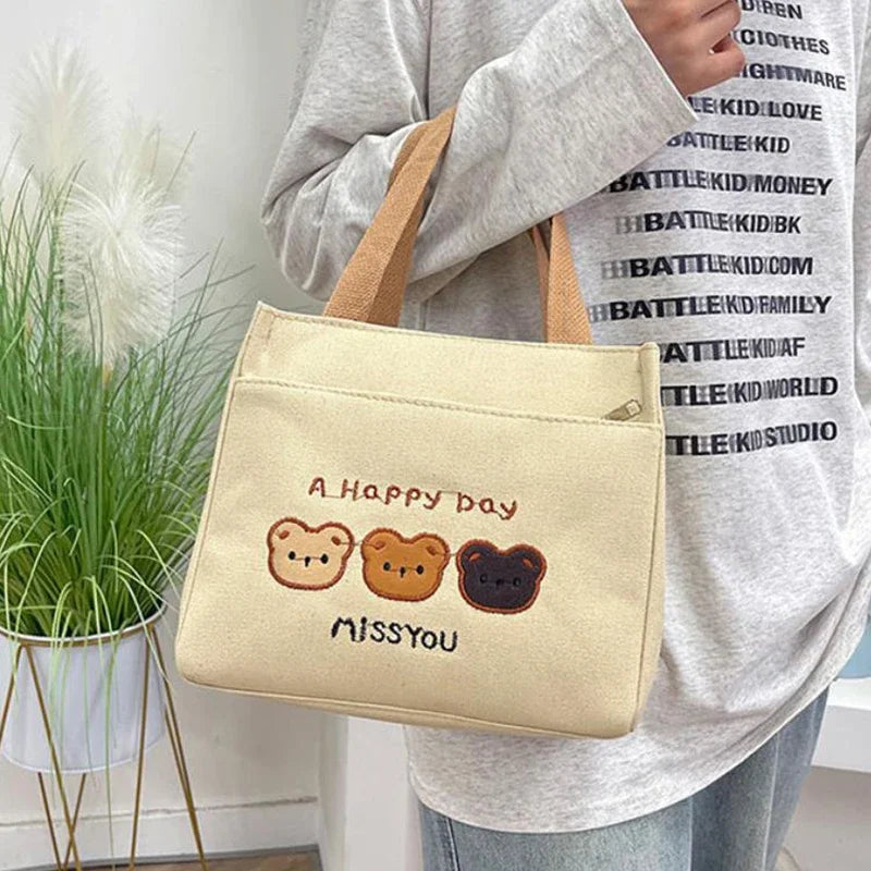Person holding a beige kawaii tote bag with bear illustrations and text, standing indoors.