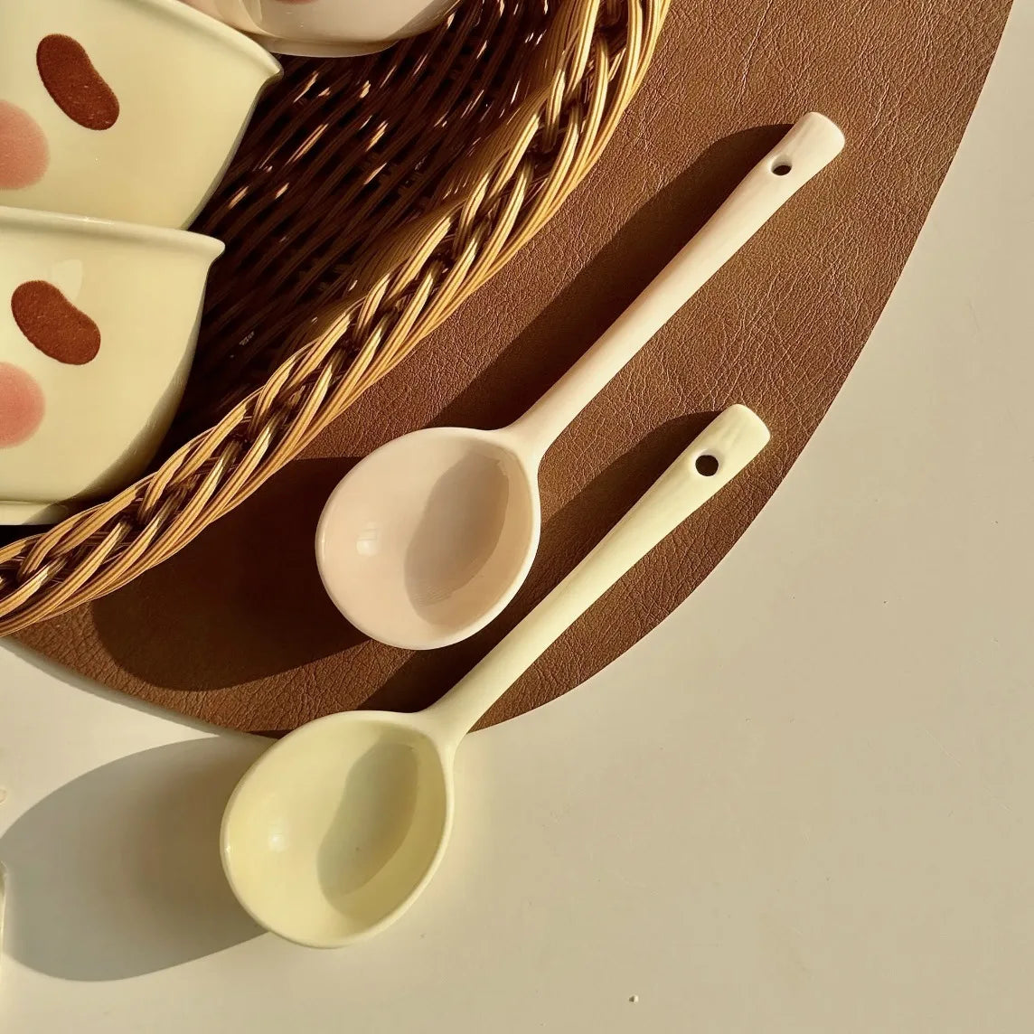 Two ceramic kawaii spoons on a textured surface with a woven basket in the background.