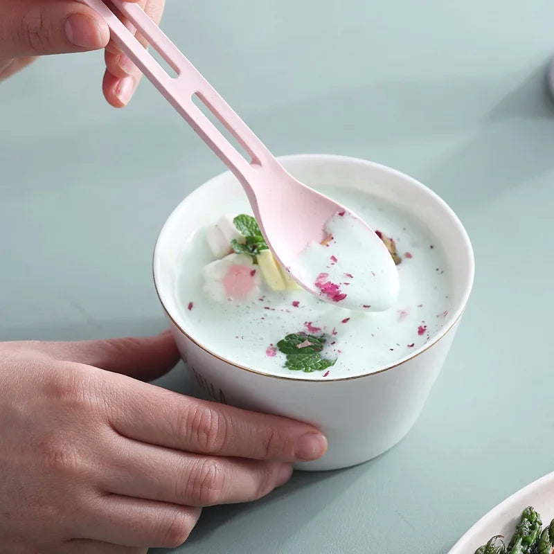 Person holding a pink kawaii utensil over a bowl of soup with vegetables on a light blue background