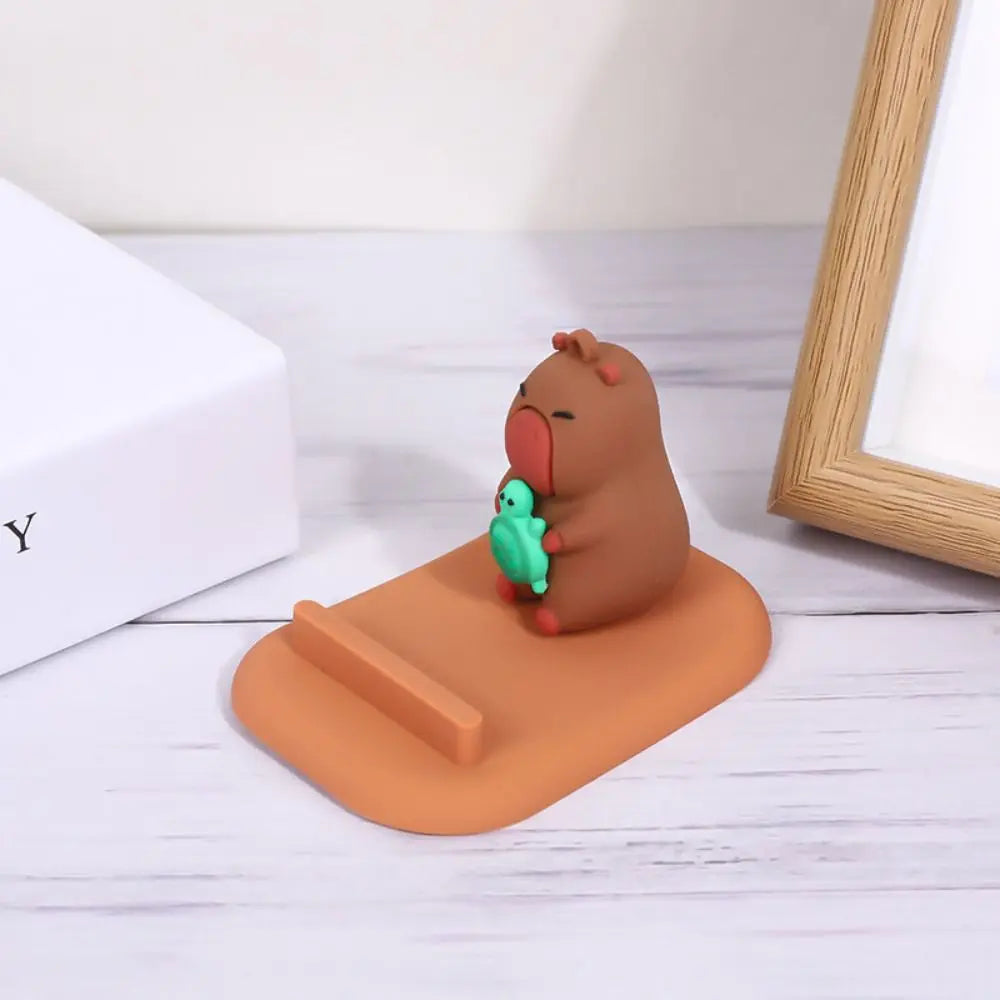 Brown capybara kawaii phone holder holding a green leaf on an orange stand with a white background