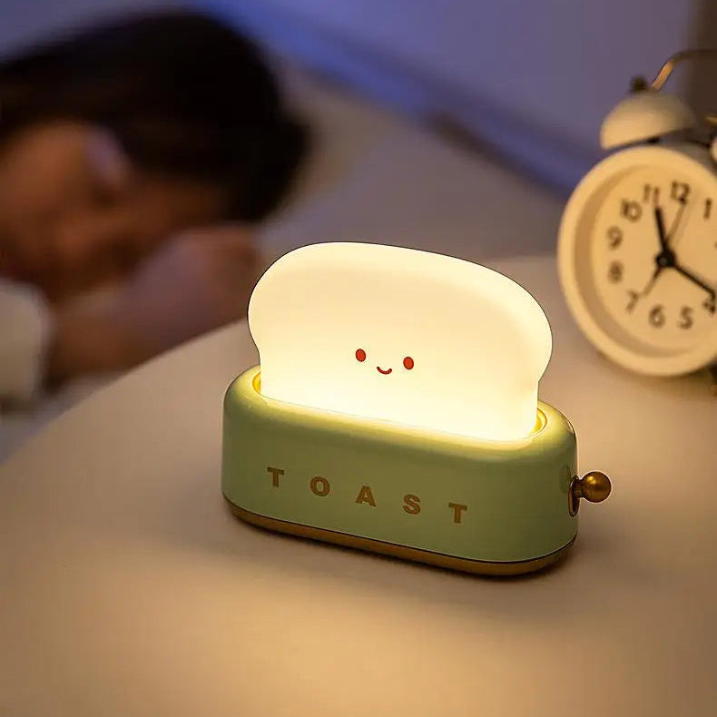Light-up toaster-shaped kawaii night light on a bedside table with a person and alarm clock in the background.