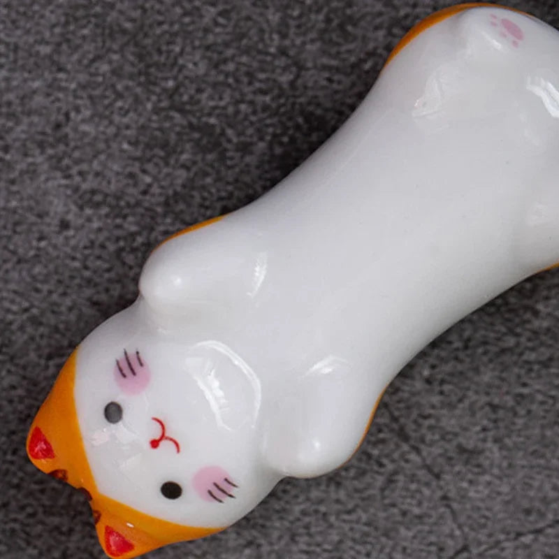 White ceramic cat-shaped kawaii chopstick holders with orange background on a textured gray surface