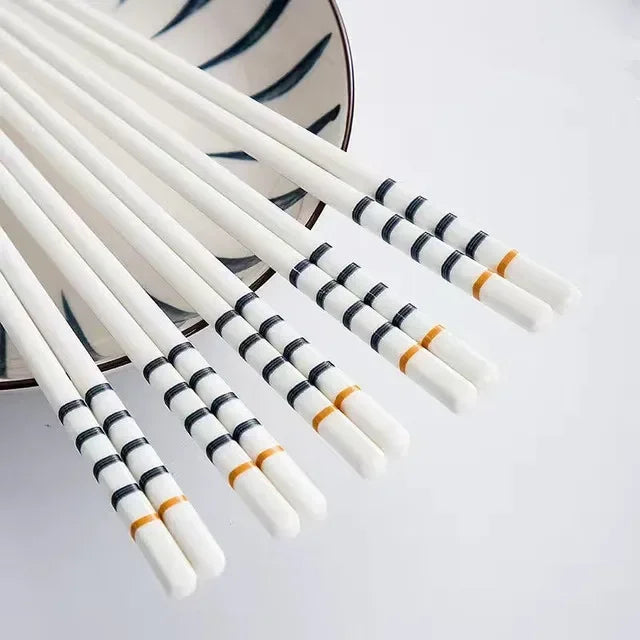 Set of white kawaii chopsticks with black and orange patterns on a light gray background