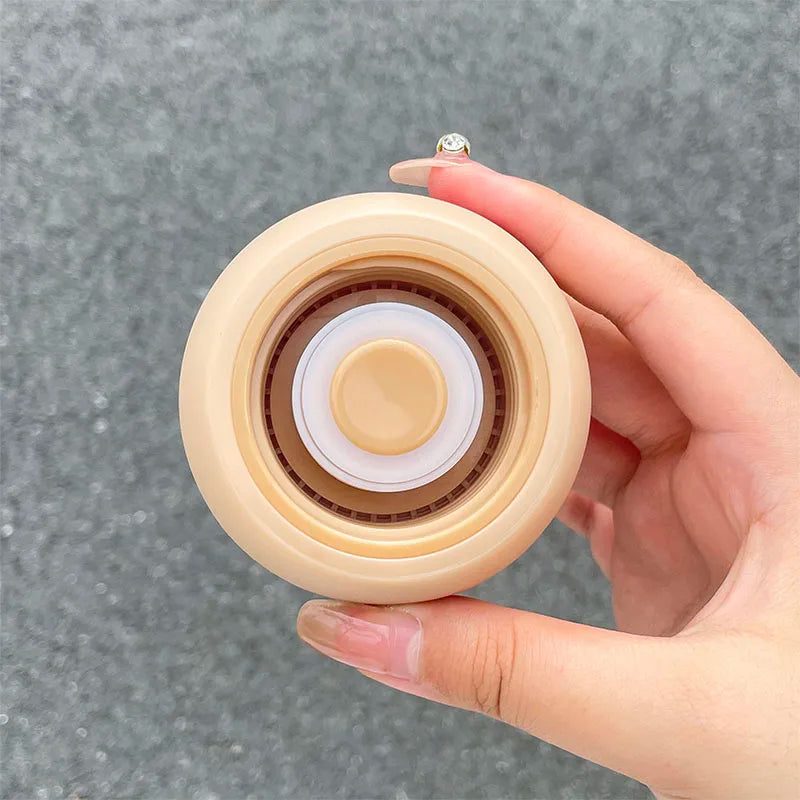 Hand holding a round, beige-colored kawaii water bottle with a textured surface against a gray background