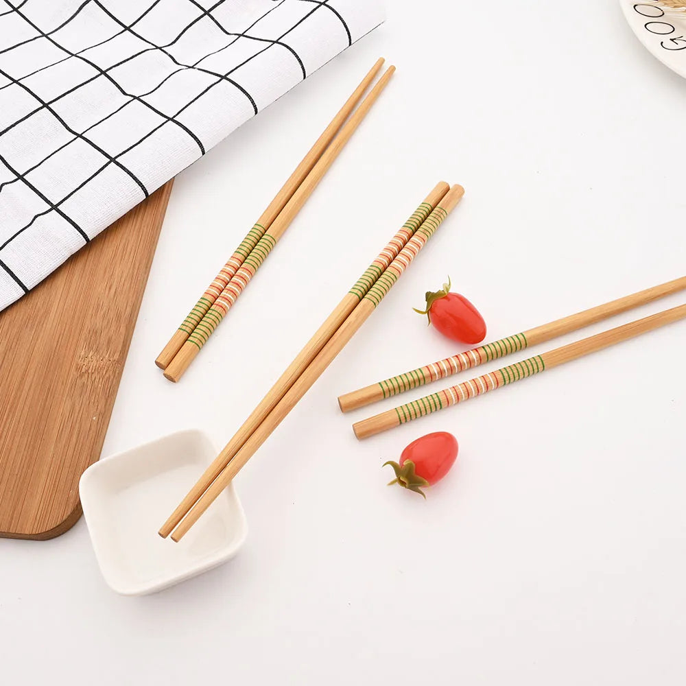 Set of bamboo kawaii chopsticks with decorative handles on a white surface with tomatoes and a cutting board.