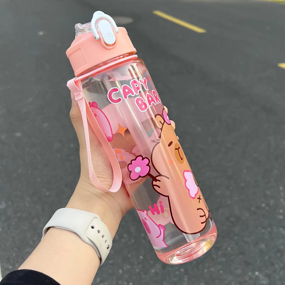 Pink kawaii water bottle with cartoon character held by a person on a dark surface