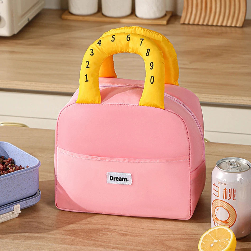 Pink kawaii lunch bag with yellow handle featuring numbers, placed on a wooden surface with a can and container.