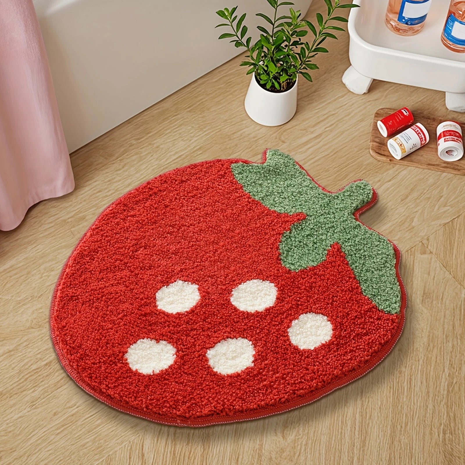 Red strawberry-shaped kawaii rug on a wooden floor with a plant and small items in the background.
