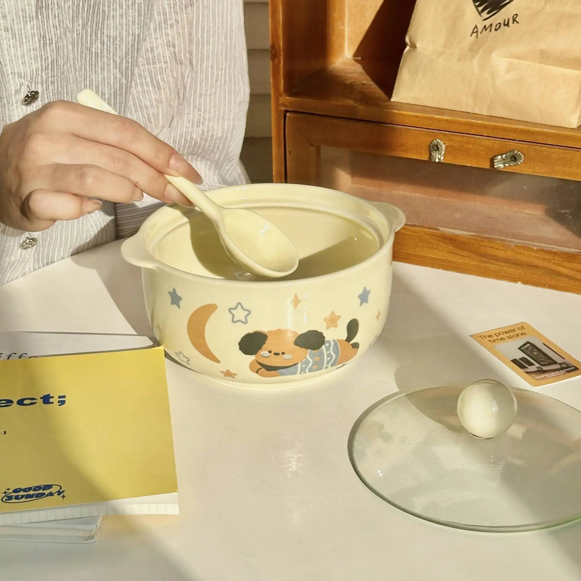 Person holding a spoon over a kawaii ramen bowl with cartoon design on a table.