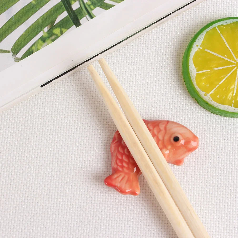 Fish-shaped kawaii chopstick holders with wooden chopsticks on a white surface with a lemon slice and green leaves in the background.