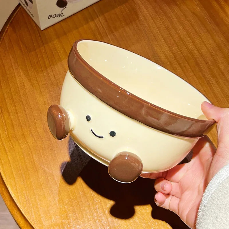 Ceramic kawaii bowl with a smiley face design held by a hand on a wooden surface