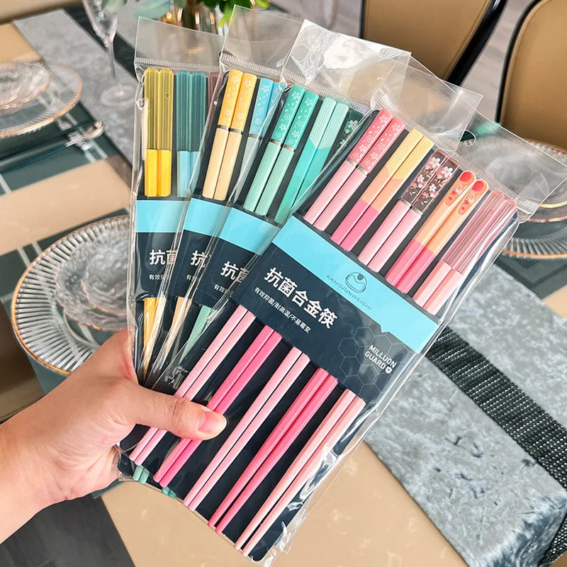 Packaged colorful kawaii chopsticks held by a hand with a dining table in the background