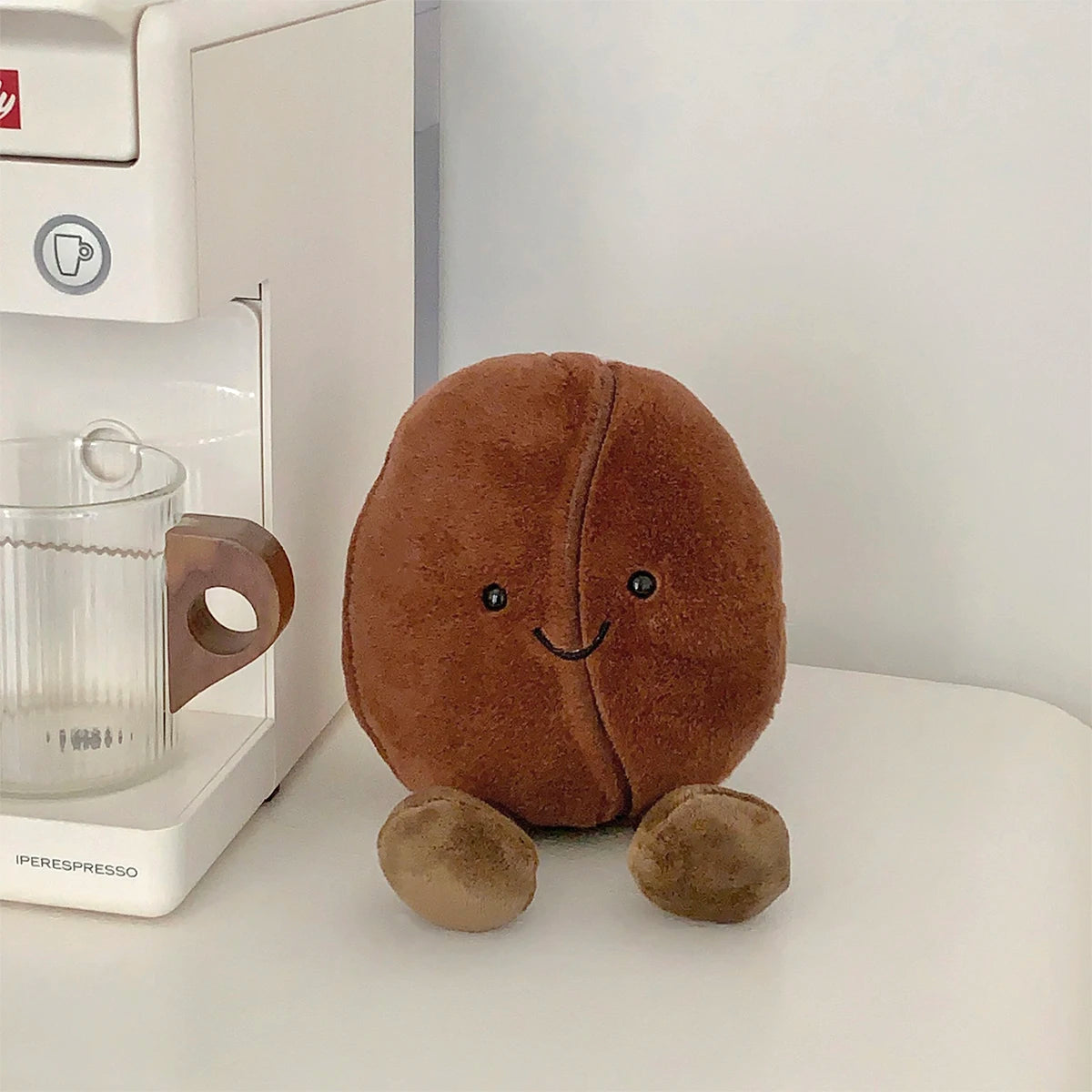 Kawaii plush coffee bean toy next to a Perespresso coffee machine on a white surface.