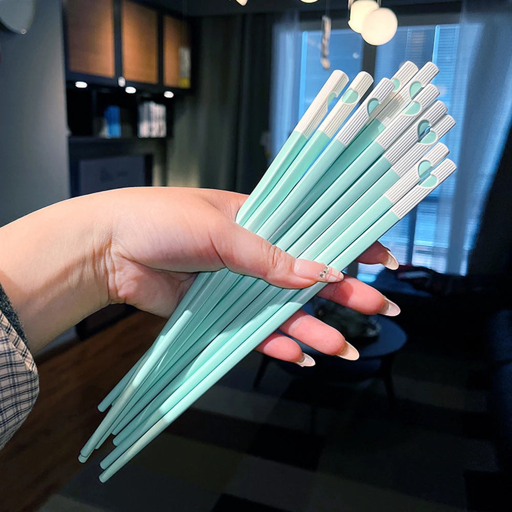 Hand holding a bundle of kawaii chopsticks with white ends indoors.