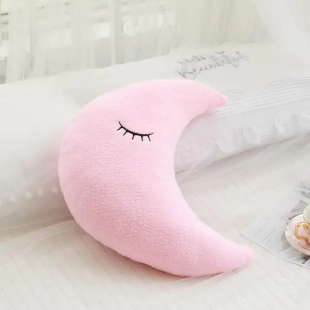 Pink crescent moon-shaped kawaii pillow with a face on a white surface