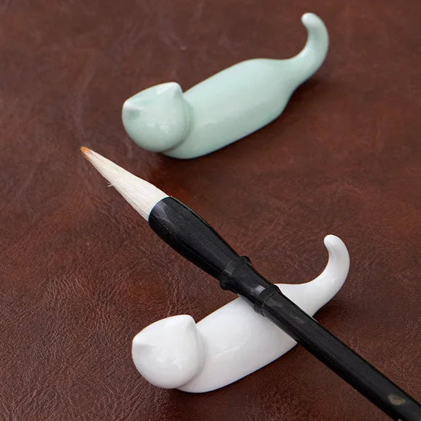 Two ceramic animal-shaped kawaii chopstick holders with a brush on a brown textured background