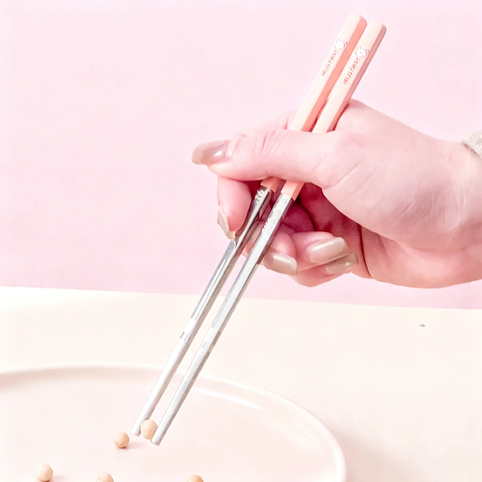 Hand holding rose gold kawaii chopsticks against a pink background