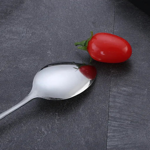 Kawaii utensils with a red berry on a dark surface