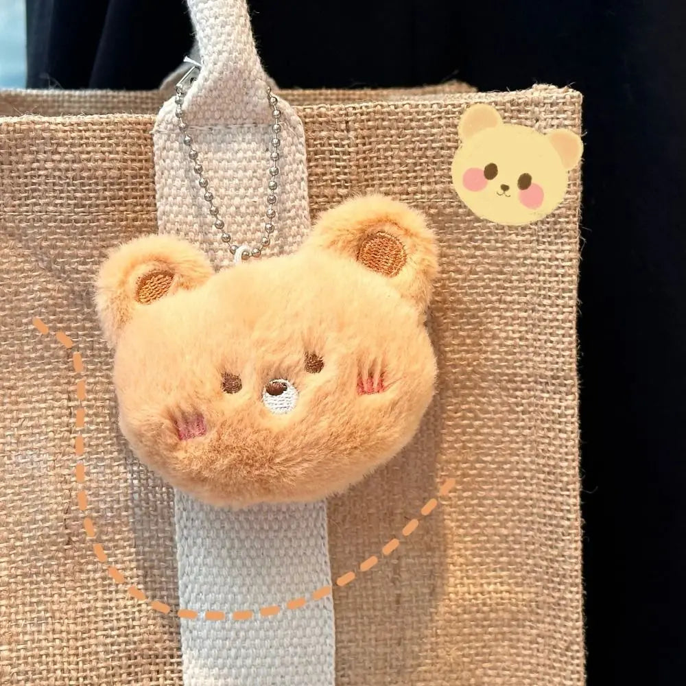 Plush kawaii bear keychain attached to a textured bag with a small bear sticker on a dark background