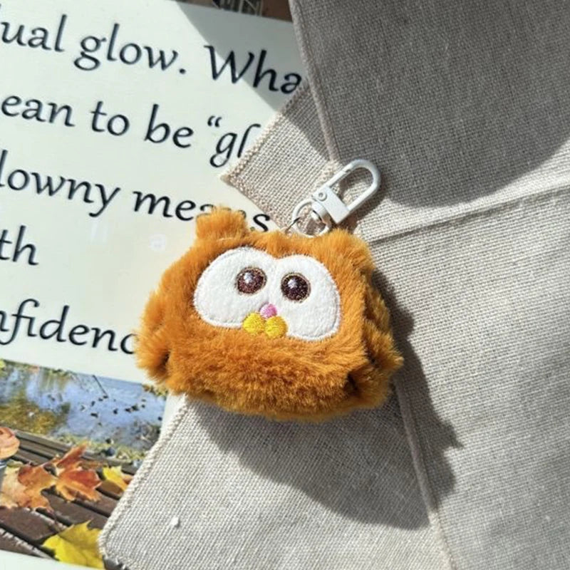 Plush kawaii owl keychain attached to a bag with text and autumn leaves in the background