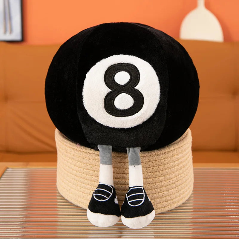 Kawaii plush toy resembling a billiard ball with the number 8 on a woven stool, sitting on a wooden floor.