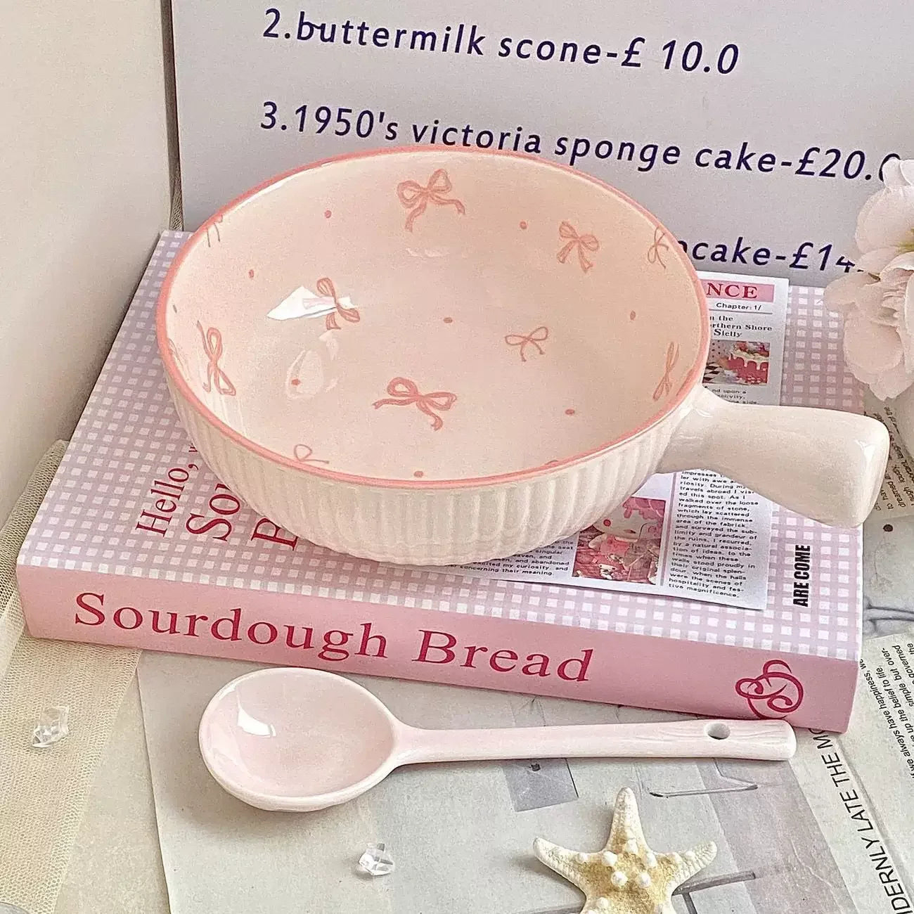 Pink ceramic kawaii ramen bowl with handle and matching spoon on a book titled 'Sourdough Bread'.