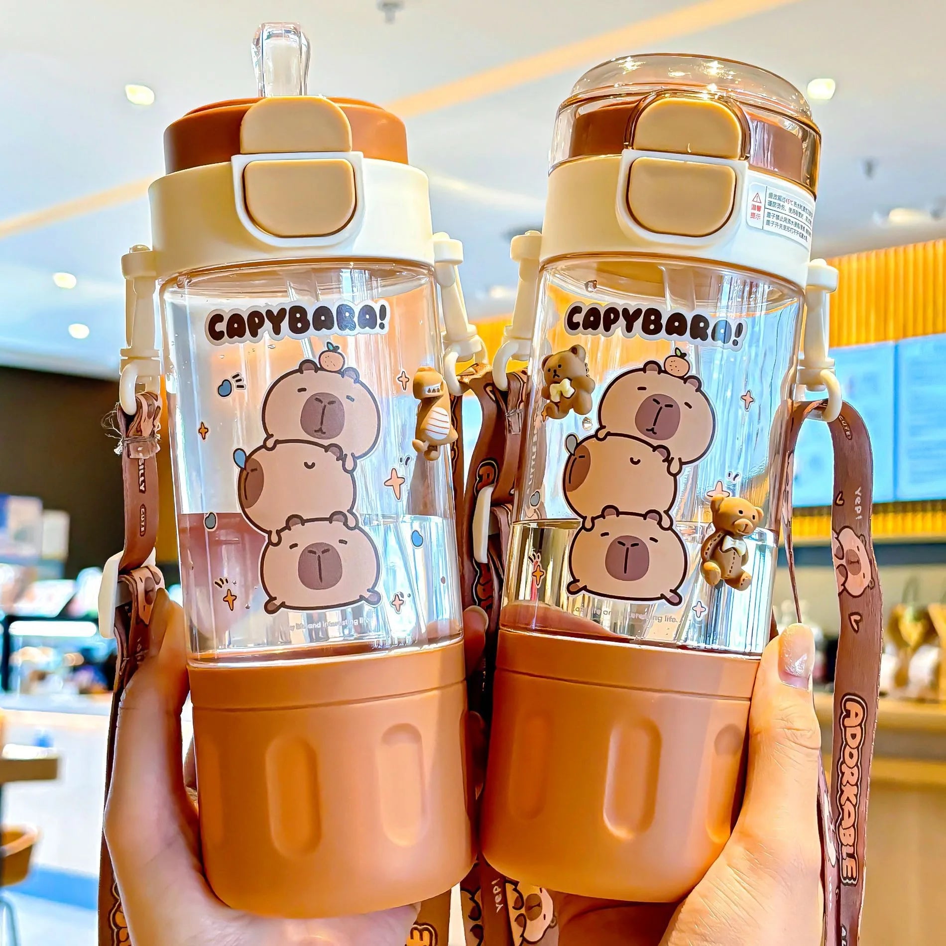 Two kawaii capybara water bottles held in hands with a blurred indoor background