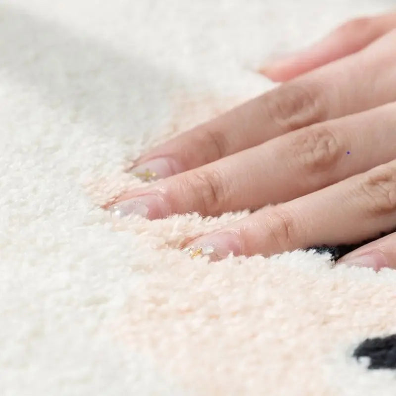 Close-up of a hand touching a soft, white kawaii rug