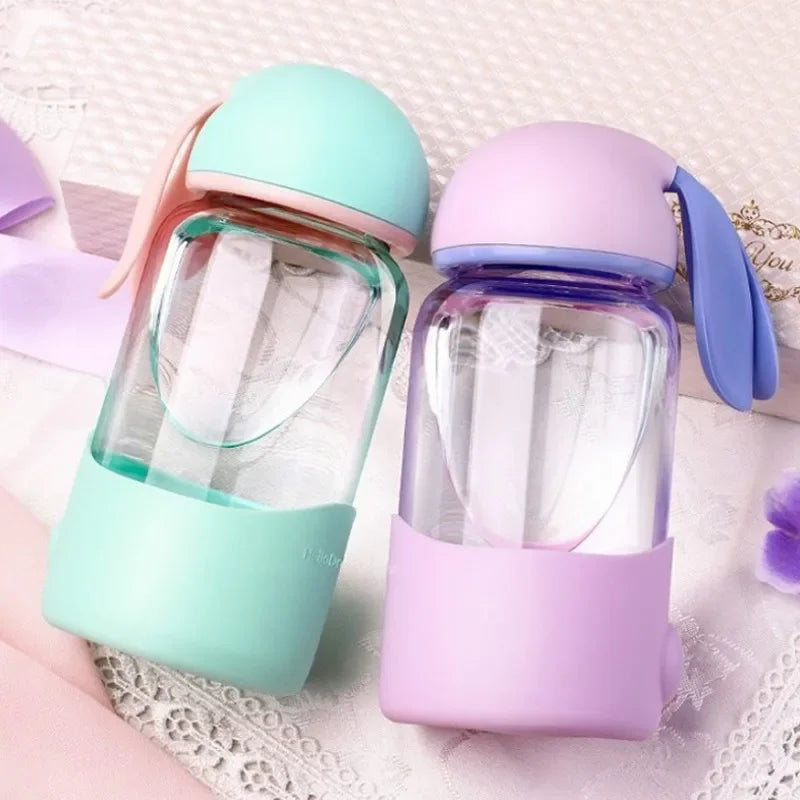 Two colorful glass kawaii cups with silicone sleeves on a textured surface
