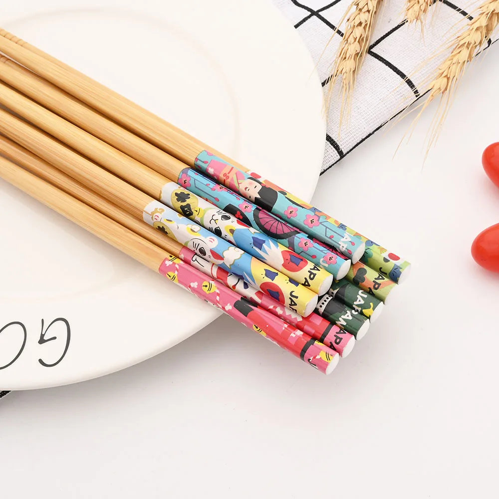 Set of colorful patterned kawaii chopsticks on a white surface with a plate and wheat stalks in the background.