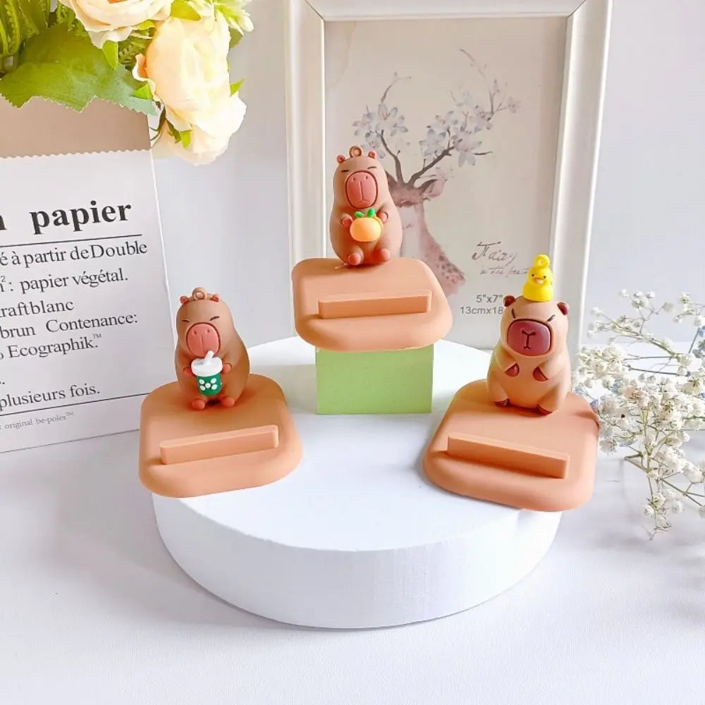 Three small kawaii phone holders on a white stand with a decorative background