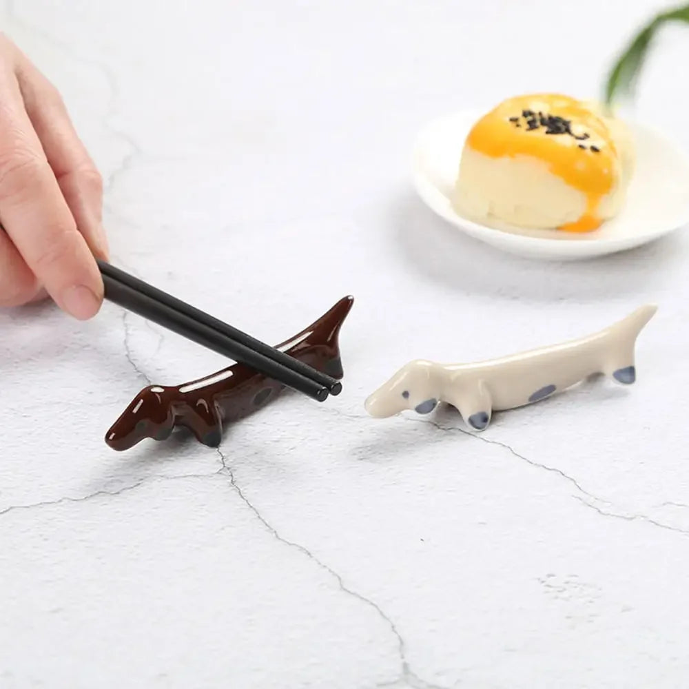 Chopsticks held by a hand with animal-shaped kawaii chopstick rests on a light surface.