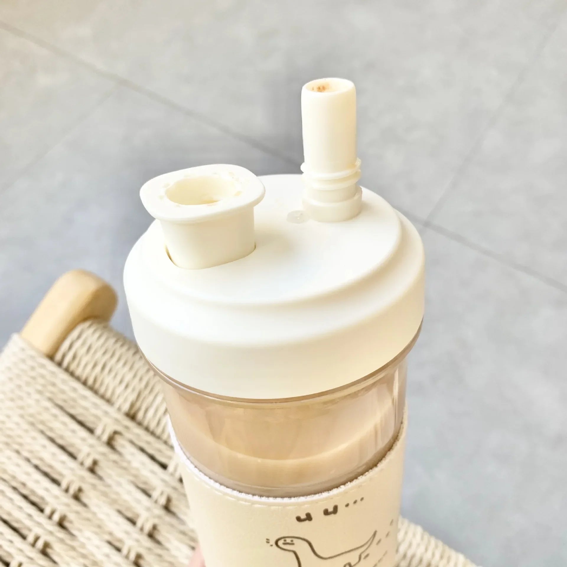 Beige silicone straw lid on a kawaii water bottle with a straw, placed on a woven surface.
