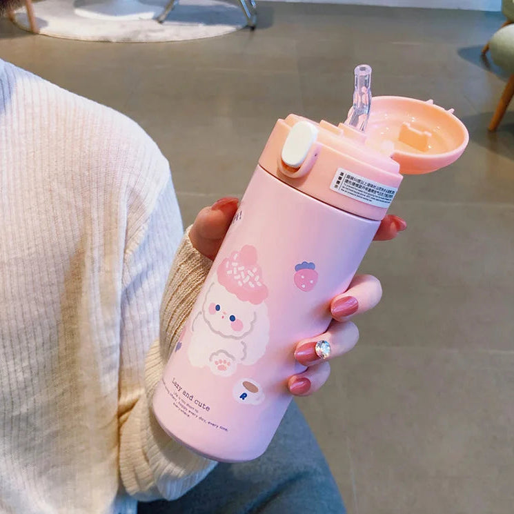 Person holding a pink kawaii water bottle with cartoon character design indoors.